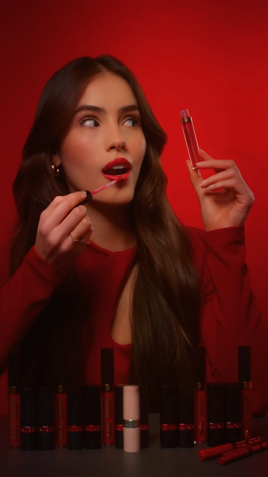 Beatriz aplicando batom em cenário vermelho